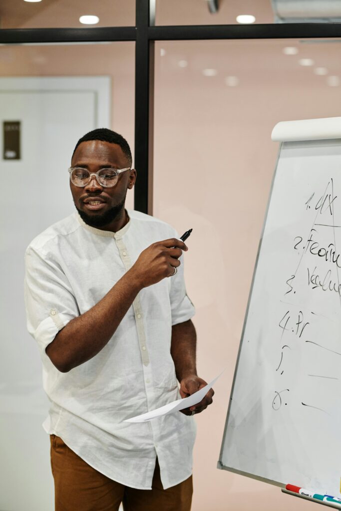 Man presenting at whiteboard in an office, explaining concepts with confidence.