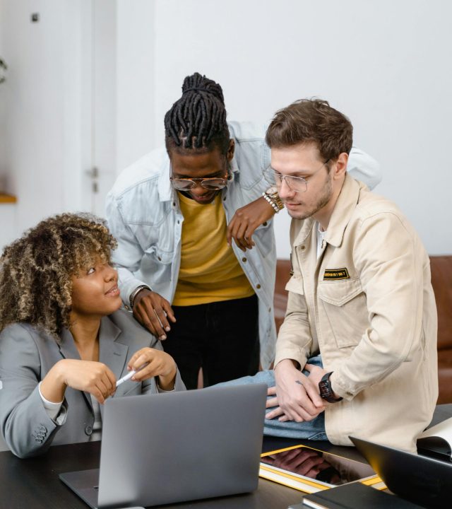 A diverse group of colleagues engaged in a collaborative project discussion around a laptop.